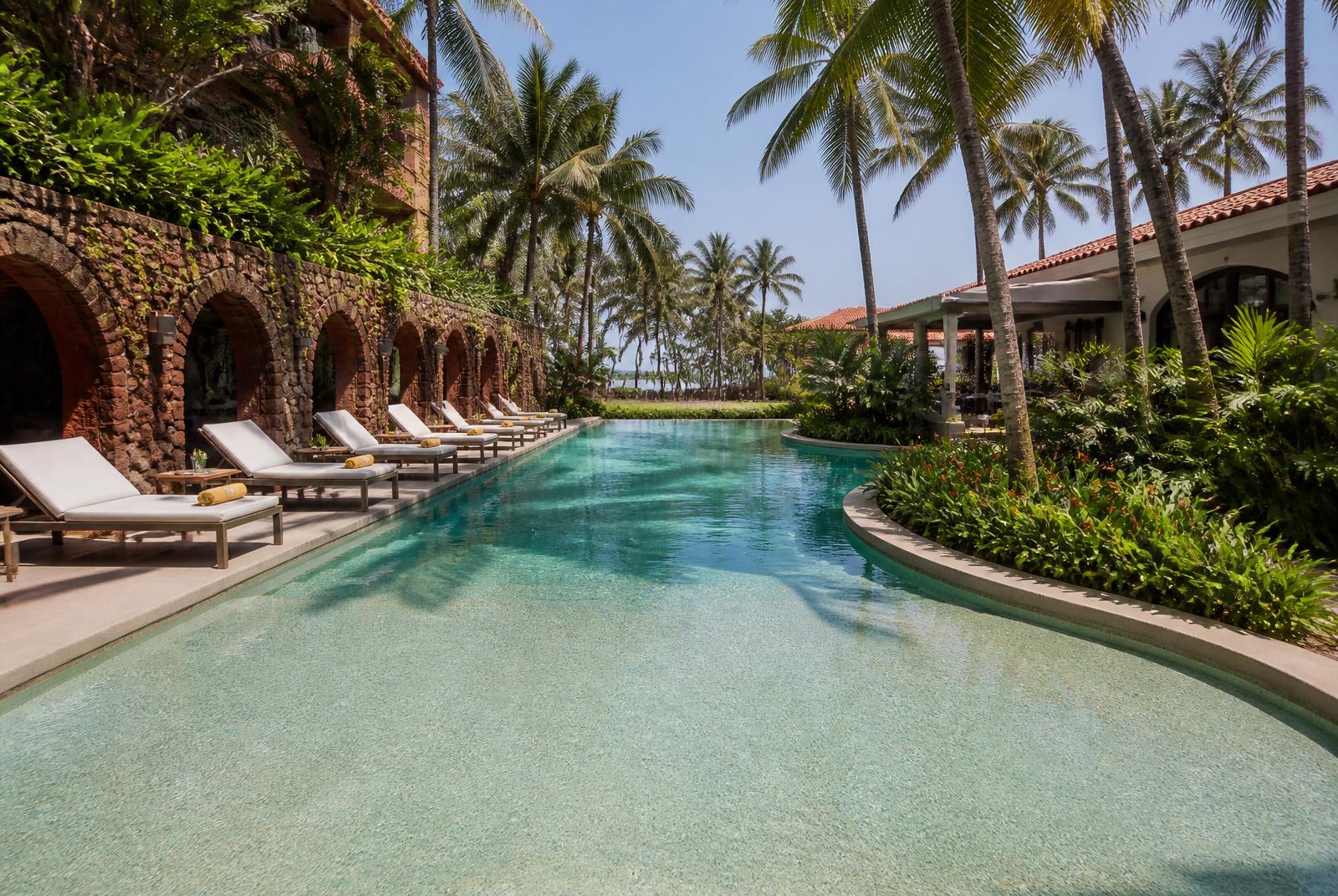 Reinforced membrane liner resort pool in Goa with laterite walls and palms